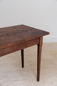 an old wooden table sitting on top of a carpeted floor next to a white wall