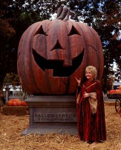 a woman standing next to a carved pumpkin