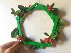 a person is making a paper wreath with leaves and berries