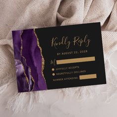 a black and purple wedding card with gold foil on the front, sitting on a white blanket