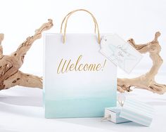 a welcome sign and gift bag sitting next to some driftwood