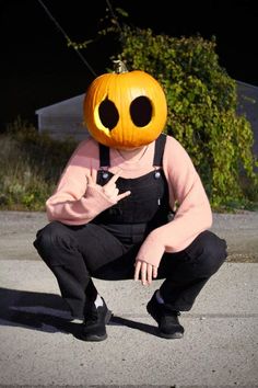 a person wearing a pumpkin mask sitting on the ground with their hand in his pocket