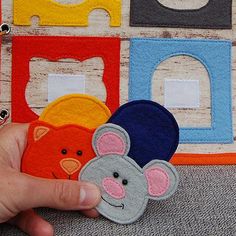 a hand is holding two felt mouses in front of a wall with colorful blocks