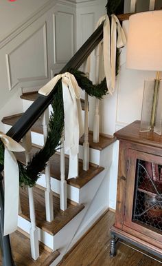 a staircase decorated for christmas with white ribbon and greenery on the bannister