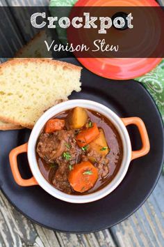 a black plate topped with a bowl of stew next to a piece of bread on top of a wooden table