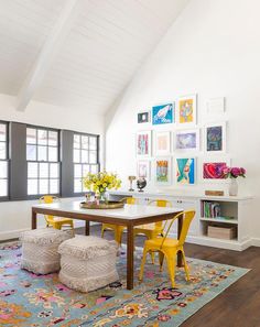 a dining room table with yellow chairs and pictures on the wall above it, along with two stools