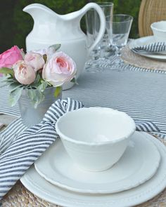 the table is set with white dishes and pink roses