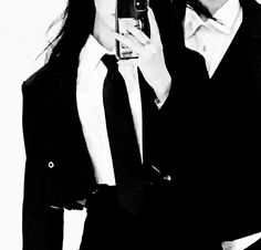 two women in suits are taking a selfie with their cell phone while wearing glasses