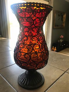 a red and black vase sitting on top of a table next to a window in a room