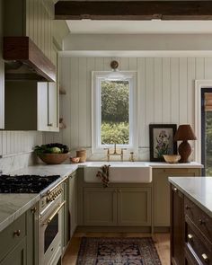 a kitchen with green cabinets and white counter tops, an area rug on the floor