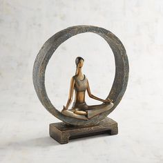 a statue of a woman sitting in a yoga pose on top of a circular object