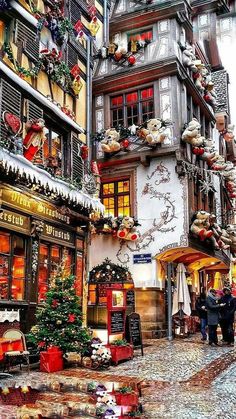 a painting of people walking down the street in front of buildings with christmas decorations on them