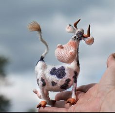 a hand holding a small toy cow in it's right hand, with clouds in the background