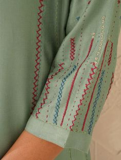 a woman wearing a green shirt with red and blue stitching