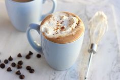 two blue mugs filled with hot chocolate and whipped cream on top of a white counter