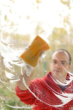 a man holding a sponge in front of a window with water droplets on the glass