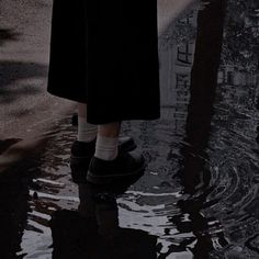 a person standing in the water with their feet up and wearing black slip ons