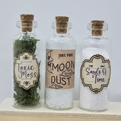 three bottles filled with sand and seaweed on top of a wooden shelf next to each other