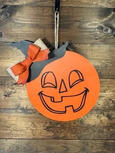 an orange paper pumpkin hanging on a wooden wall with a bow around it's neck