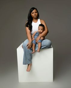 a woman sitting on top of a white block holding a baby