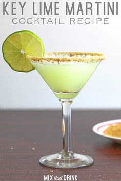 a green drink with a slice of lime on the rim next to a small plate