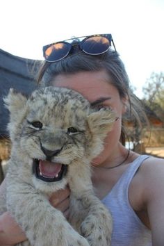 a woman holding a baby lion cub in her arms with sunglasses on it's head