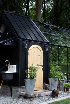 a small black shed with a sink and potted plants