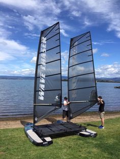 two people standing on the grass next to a sailboat