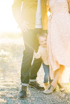 a man and woman standing next to a small child in front of a tree with the sun shining on them