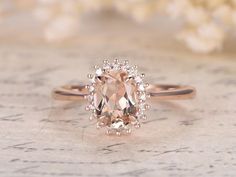 an oval cut peach morganite sits on top of a white surface with flowers in the background