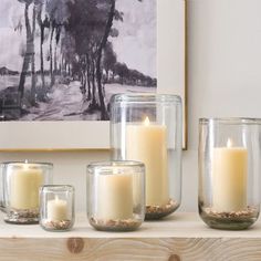 some candles are sitting on a shelf in front of a painting