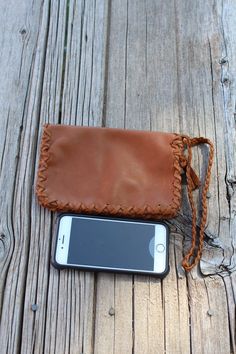 a cell phone sitting in a brown leather case on top of a wooden table next to a wallet