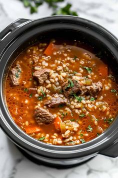 a pot filled with meat and barley soup on top of a marble countertop next to parsley