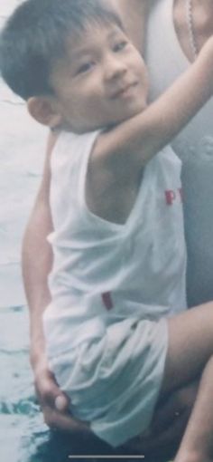 a young boy is hugging his mother in the water while she holds her arm around him