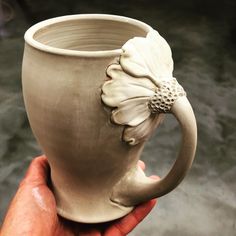 a hand holding a ceramic mug with a flower on it