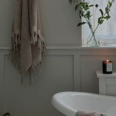 a white bath tub sitting under a window next to a vase with flowers on it