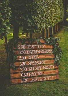 a wooden sign sitting in the middle of a lush green field next to tall trees