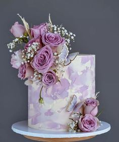 a pink and white cake with purple flowers on top is sitting on a table in front of a gray wall