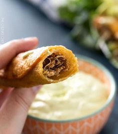 a person is holding up a pastry in front of a bowl of dip