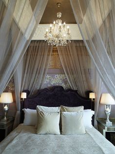 a bed with white sheets and pillows under a chandelier