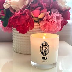 a white candle sitting on top of a table next to pink and red flowers in a vase