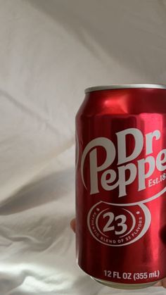 a hand holding a can of dr pepper soda on a white sheeted background,