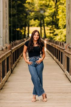 a woman standing on a bridge with her hands in her pockets and smiling at the camera