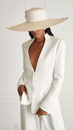 a woman wearing a white suit and wide brimmed hat with her hands on her hips