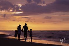 a family walking on the beach at sunset