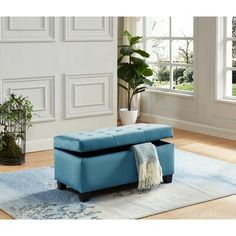 a blue ottoman sitting on top of a rug in front of a white wall and windows