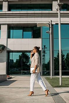 a woman walking down the street while talking on her cell phone by an office building