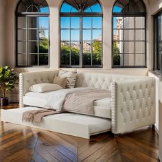 a large white bed sitting in front of two windows on top of a hard wood floor