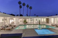 an outdoor swimming pool with lounge chairs and palm trees in the background at night time