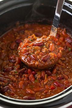 a ladle full of chili and beans in a slow cooker